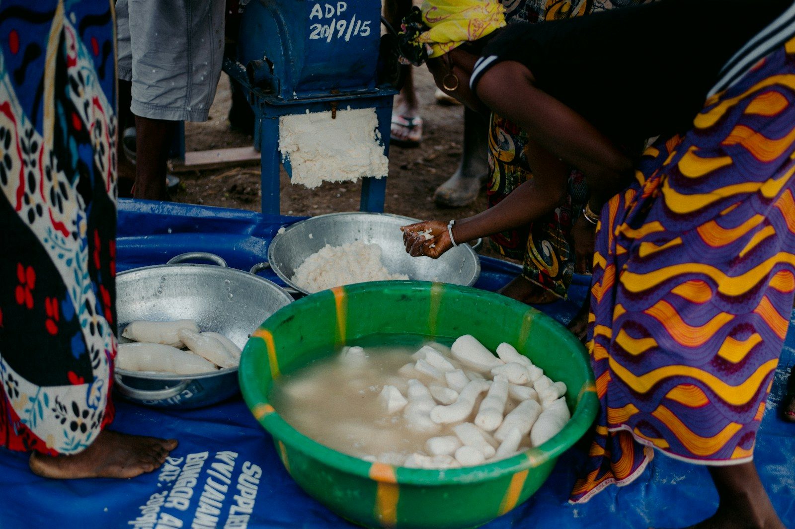 peeled cassava soaking in a green bowl of water beside a cassava grater