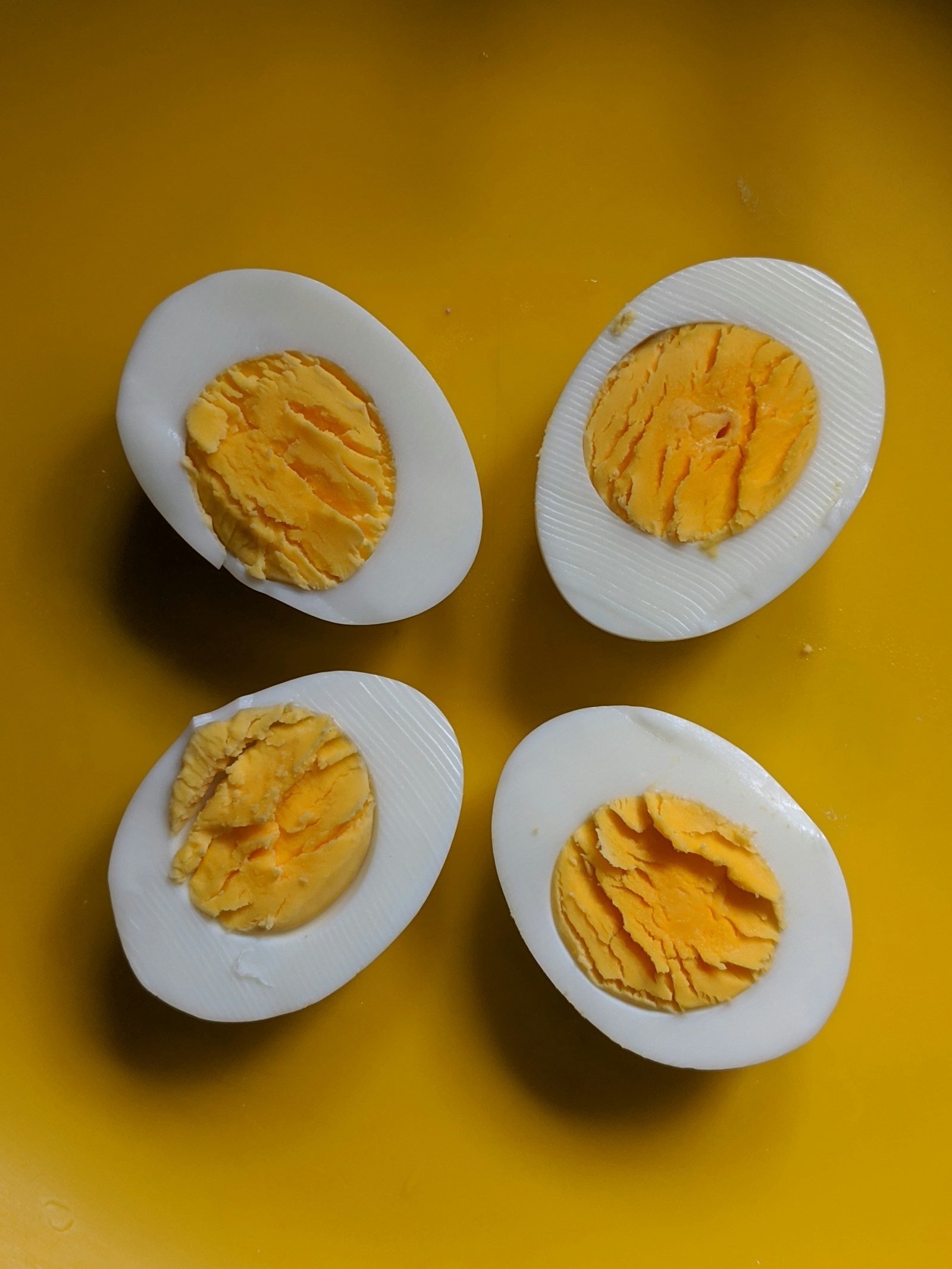 four halves of two boiled eggs on a yellow plate